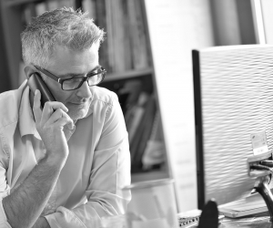 A business man at a computer grinning while on the phone